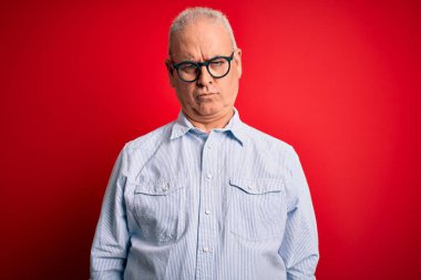 Orta yaşlı, beyaz, sıradan çizgili gömlek giyen, kırmızı arka planda gözlüklü, bunalımlı, sıkıntılı, sinirli ve korkmuş bir adam. Üzücü ifade.