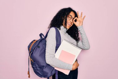 Genç Afro-Amerikan kıvırcık saçlı, sırt çantası takan ve gülümseyen gözlüklü bir kadın.