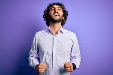 Mor arka plan üzerinde duran sakallı, genç ve yakışıklı bir iş adamı sinirli ve öfkeli çığlıklar atıyor, öfkeyle bağırıyor. Öfke ve agresif kavram.