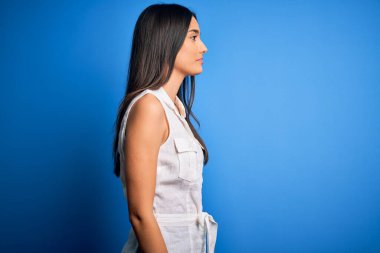 Genç, güzel esmer bir kadın, mavi arka planda rahat bir görünüm takınıyor, rahat bir görünüm takınıyor, kendine güvenen bir gülüşü var..