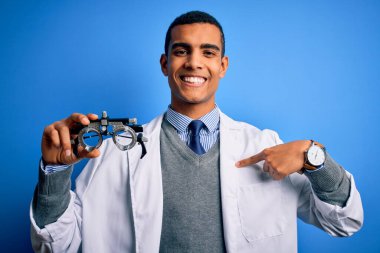 Yakışıklı afro-amerikan optik adam mavi arka planda optometri gözlüğü tutuyor.