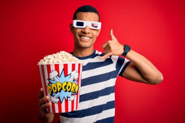 Genç ve yakışıklı Afro-Amerikalı adam film izliyor 3D gözlükler takıyor patlamış mısırlar yiyor telefonla el ve parmaklarıyla jest yapıyor telefonda konuşuyor gibi. İletişim kavramları.