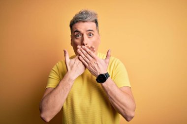 Sarı arka plan üzerine sarı tişört giyen genç ve modern bir adam yanlışlıkla elleri ile ağzını kapatırken şok oldu. Gizli konsept.