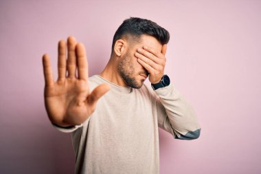 Genç, yakışıklı bir adam, pembe arka planda dikilip ellerle gözlerini kapatıyor ve hüzünlü ve korku dolu bir ifadeyle jestleri durduruyor. Utanç verici ve olumsuz bir kavram..