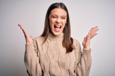 Genç ve güzel esmer bir kadın beyaz arka planda dikilmiş çılgın ve çılgın başarısını kutluyor kolları havada ve gözleri kapalı heyecanla bağırıyor. Kazanan konsept