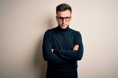 Gözlük takan yakışıklı beyaz bir adam izole edilmiş arka plan şüphecisi ve gergin kolları çaprazlanmış yüz ifadesini tasvip etmeyen sıradan bir kazak giyiyor. Negatif kişi.