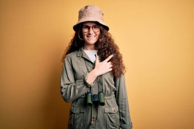 Tatilde olan genç, güzel bir turist kadın kaşif şapkası ve dürbün takıyor. Yüzünde mutlu ve doğal bir ifadeyle, elleri ve parmaklarıyla gülümsüyor.
