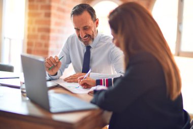 Mutlu ve kendinden emin gülümseyen iki orta yaşlı iş adamı. Ofiste dizüstü bilgisayarla gülümseyerek birlikte çalışıyoruz.