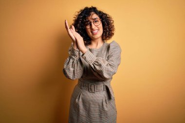 Güzel bir Arap iş kadını. Elbise ve gözlük takıyor. Sarı arka planda duruyor.