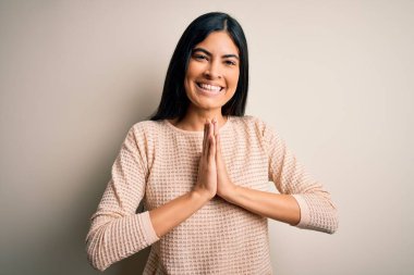 Zarif pembe bir süveter giyen genç ve güzel bir kadın izole edilmiş arka planda dua ediyor ellerle birlikte af diliyor kendinden emin bir şekilde gülümsüyor..