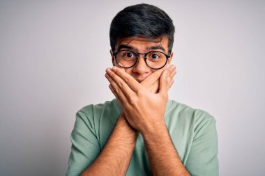 İzole edilmiş beyaz arka plan üzerine gündelik tişört ve gözlük takan genç yakışıklı adam yanlışlıkla ağızlarını kapatarak şok etti. Gizli konsept.