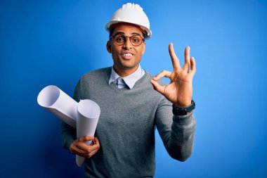 Güvenlik kaskı takan genç Afrikalı Amerikalı mimar elinde planlarla tamam işareti tutuyor, mükemmel bir sembol.