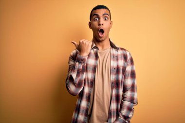 Sarı arka planda dikilen rahat gömlekli, genç, Afro-Amerikan bir adam. El parmağı yana dönük, ağzı açık, şaşkın bir ifade..