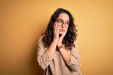 Kıvırcık saçlı, çizgili tişörtlü ve sarı arka planda gözlüklü güzel bir kadın. Yüzü, depresyonu ve üzüntüyü örten yorgun elleri var.