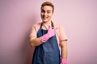 Genç, kızıl saçlı, ev işi yapan, önlüklü, eldivenli, neşeli yüzlü, elleri ve parmaklarıyla gülümseyen, mutlu ve doğal bir ifade takınan genç bir adam.