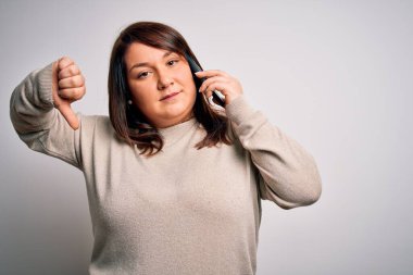 Güzel, iri yarı bir kadın, izole edilmiş arka planda akıllı telefondan konuşuyor. Kızgın yüzlü, negatif işaretli, baş parmakları aşağıda, reddedilme kavramından hoşlanmıyor.