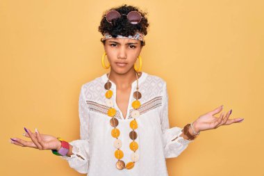 Güneş gözlüğü takan, aksesuar takan, kolları açık ve kafası karışmış Afro-Amerikan bir kadın..
