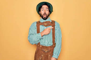 Almanya festivali için geleneksel Alman Ekim Festivali kıyafeti giyen yakışıklı genç adam parmağını yana doğru göstererek şaşırdı, ağzı açık şaşkın bir ifade takındı..