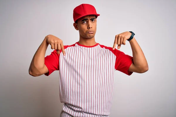 若いハンサムなアフリカ系アメリカ人のスポーツマンは 縞模様の野球Tシャツとキャップを身に着けている指で方向を示す 悲しいと動揺を下に指して 不幸と落ち込んで — ストック写真