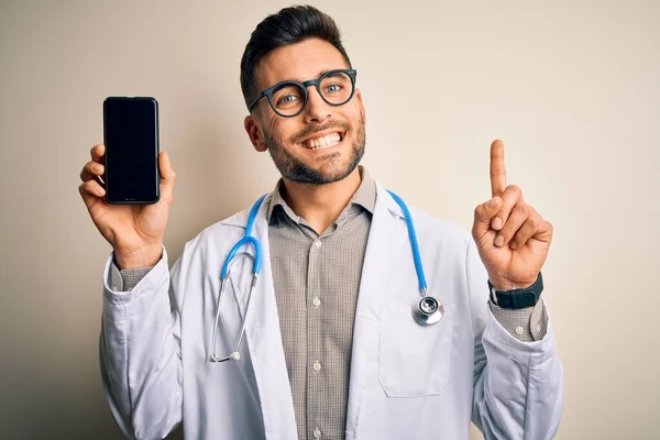 Młody Lekarz Noszący Stetoskop Pokazujący Ekran Smartfona Odosobnionym Tle Zaskoczony — Zdjęcie stockowe