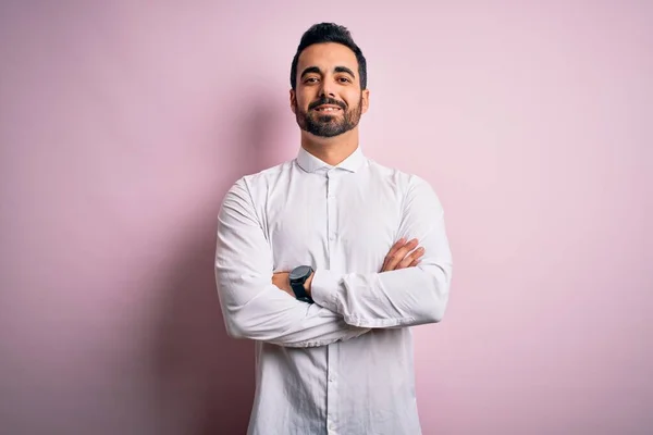 Young handsome man with beard wearing casual shirt standing over pink background happy face smiling with crossed arms looking at the camera. Positive person.