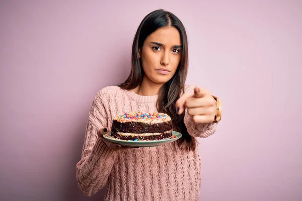 若いです美しいブルネットの女性を保持誕生日おいしいケーキ以上ピンクの背景指摘に指でカメラとあなたに 手のサイン 正と自信を持ってジェスチャーからフロント — ストック写真