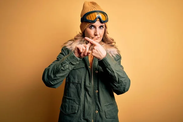 中年漂亮的金发滑雪者女人穿着雪地运动鞋和滑雪护目镜 拒绝用手指交叉表示否定的手势 — 图库照片