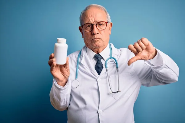 Starszy Siwowłosy Lekarz Trzyma Tabletki Farmaceutyczne Niebieskim Tle Wściekłą Twarzą — Zdjęcie stockowe