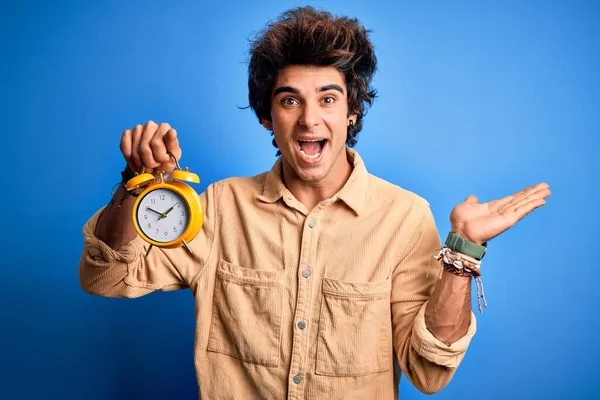 Joven Hombre Guapo Sosteniendo Despertador Pie Sobre Fondo Azul Aislado — Foto de Stock