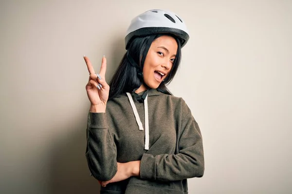 若い美しい中国の女性が孤立した白い背景の上に自転車のヘルメットを身に着けている幸せな顔が勝利のサインを行うカメラでウィンクと笑みを浮かべて 第二番 — ストック写真