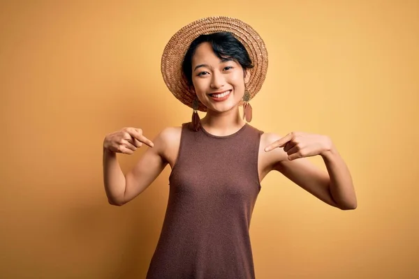 年轻美丽的亚洲女孩 身穿休闲装 头戴一顶帽子 头戴黄褐色相间的背景 面带微笑 用手指指着自己 自豪而快乐 — 图库照片