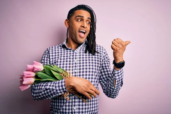 若いですアフリカ系アメリカ人アフロロマンチックな男とともにフリーピンクチューリップの花束を持っています笑顔で幸せな顔見ますと指で側面を指していますアップ — ストック写真