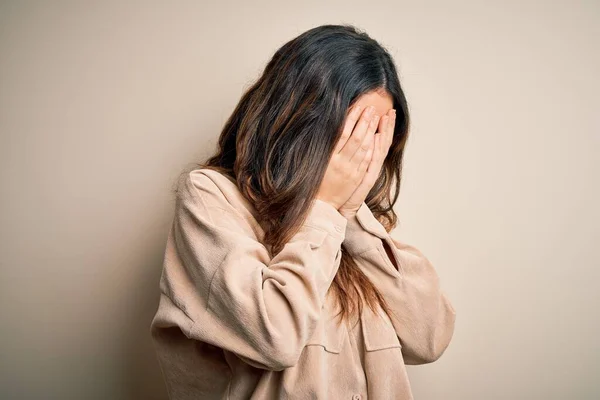 Young beautiful brunette woman wearing casual shirt standing over white background with sad expression covering face with hands while crying. Depression concept.