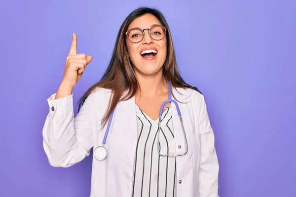 成功した考えと指を指す紫色の背景の上に聴診器や医療コートを身に着けている専門医の女性 興奮し 第一番 — ストック写真