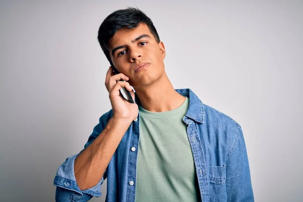 Young handsome man having conversation talking on the smartphone over white background with a confident expression on smart face thinking serious