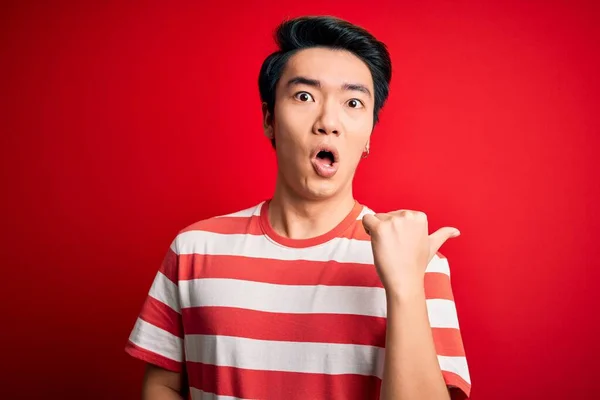Mladý Pohledný Číňan Neformálním Pruhovaném Tričku Stojící Nad Červeným Pozadím — Stock fotografie