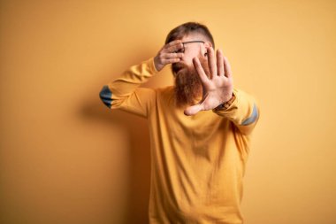 Sarı arka planda gözlüklü, sakallı, yakışıklı, kızıl saçlı, gözleri ellerle kaplayan ve üzgün ve korku ifadeli hareketler yapan yakışıklı bir adam. Utanç verici ve olumsuz bir kavram..