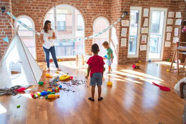 Anaokulunda bir sürü oyuncağın etrafında basketbol oynayan genç ve güzel öğretmenler ve yeni yürümeye başlayan çocuklar.
