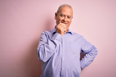 Orta yaşlı, beyaz gömlekli, pembe arka planda dikilen, kolları çapraz ve çenesi açık bir şekilde kameraya kendinden emin bir şekilde bakan yakışıklı bir adam. Olumlu düşünüyorum..