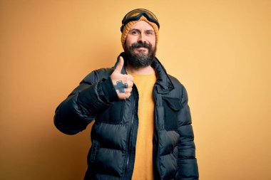 Sakallı, kar maskesi takmış, kar maskesi takmış ve kayak gözlüklü yakışıklı kayakçı elleriyle mutlu bir jest yapıyor. Kameraya bakıp başarıyı gösteren ifade onaylanıyor.