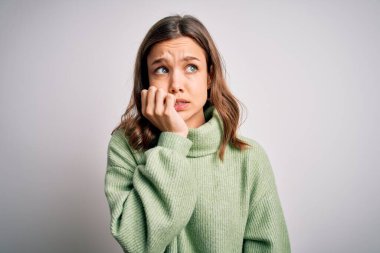 Kışlık süveter giyen genç ve güzel bir kız izole bir arka planda duruyor. Elleri ağızda, tırnaklarını yerken gergin ve stresli görünüyor. Endişe sorunu.