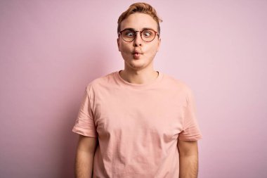 Genç, kızıl saçlı, günlük tişört giyen, izole edilmiş pembe arka planda duran dudaklı, çılgın ve komik bir jest yapan yakışıklı bir adam. Komik ifade.