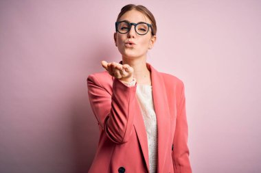 Ceket ve gözlük takan genç, güzel, kızıl saçlı bir kadın pembe arka planda kameraya bakıp havada öpüşürken güzel ve seksi görünüyor. Aşk ifadesi.