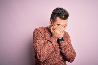 Pembe izole arka plan üzerine günlük kazak giyen yakışıklı beyaz bir adam. Ağlarken suratını ellerle kapatan üzgün bir ifade. Depresyon kavramı.