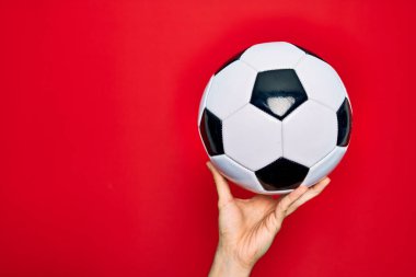 Güzel bir el futbol topunu izole edilmiş kırmızı arka planda tutuyor.