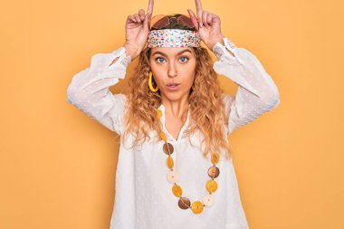 Mavi gözlü, güneş gözlüklü, aksesuar takan genç, güzel sarışın hippi kadın boynuzları gibi parmağıyla komik hareketler yapıyor.