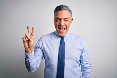 Orta yaşlı, yakışıklı, gri saçlı, şık gömlekli ve kravatlı bir iş adamı kameraya gülümseyen, parmaklarıyla zafer işareti yapan. İki numara..