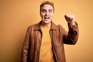 Genç, yakışıklı, deri ceket giyen, izole edilmiş sarı arka planda kızgın, kızgın, sinirli ve öfkeliyken öfkeyle bağıran bir adam. Öfke ve agresif kavram.