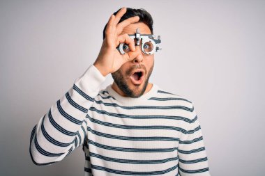 İzole edilmiş beyaz arka plan üzerinde optometri gözlüğü takan sakallı yakışıklı genç adam şaşırmış yüz ifadesiyle, parmaklarından bakan gözlerle şok olmuş bir hareket yapıyor. İnançsız ifade.