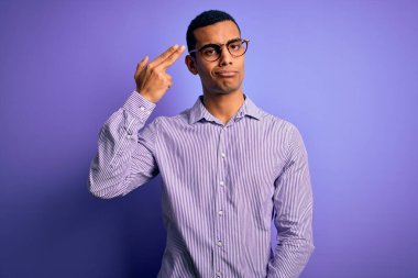 Yakışıklı afro-amerikan adam çizgili gömlek ve gözlük takıyor mor arka planda kendini vuruyor ve öldürüyor silah gibi el ve parmakları işaret ederek, intihar jesti.